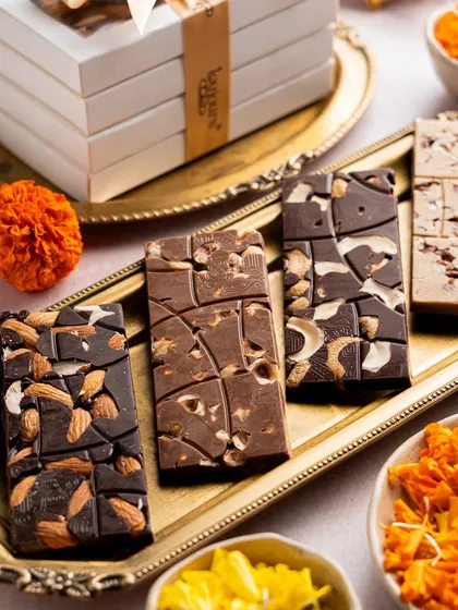 A set of four artisanal mendiant bars on a golden tray, each loaded with a different combination of roasted nuts. These Belgian chocolate bars are a simple yet luxurious treat.