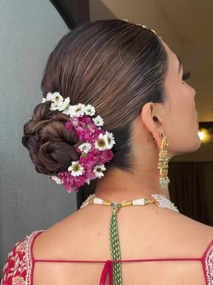 A close up of a sleek, intricately woven bridal bun. I surrounded the base with fresh pink and white daisies for a touch of natural elegance, creating a timeless look for the wedding ceremony.