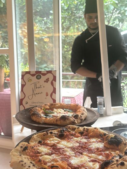 An intimate indoor pizza party setup. My chef works behind the counter with two fresh pizzas on display, showing how I can bring the full experience into your home.