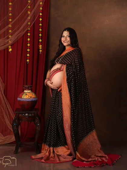 A full-length solo portrait, showcasing the beautiful drape of the black and orange saree.