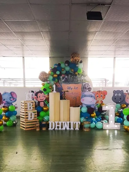A wild jungle safari theme for a first birthday. The decor features a variety of animal cutouts like a lion, monkey, and hippo, set against a backdrop of lush green and brown balloons.