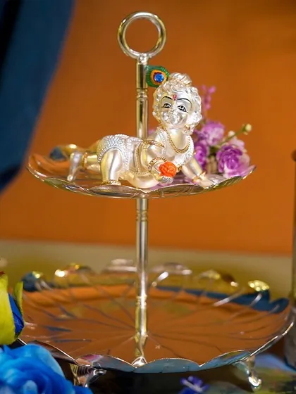 A perfect blessing for a little one, this silver-plated crawling Krishna is presented on an elegant two-tiered serving stand. It's a unique and memorable gift for a baby shower or birth announcement.