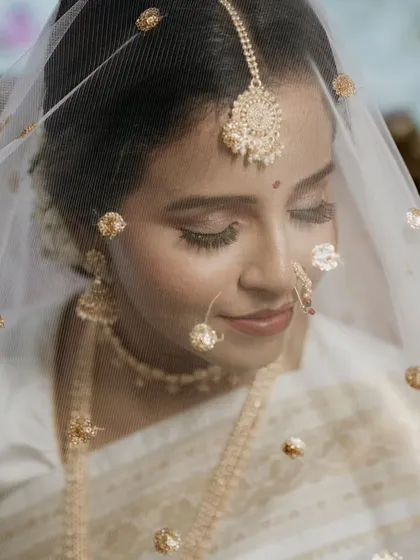 A delicate and dreamy bridal portrait. The sheer veil with golden details adds a layer of softness to this close-up shot, capturing the bride's graceful and serene beauty.