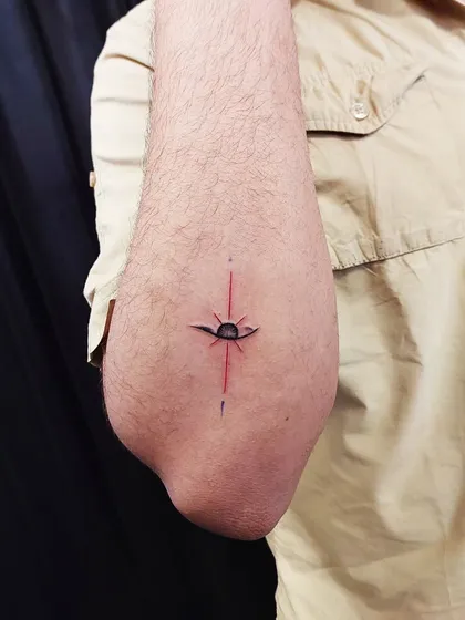 An abstract eye and sun tattoo, created with a mix of black and red ink. This minimalist piece is a unique symbol of vision and consciousness.