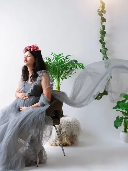 A bright and airy studio portrait of an expecting mother seated in a beautiful grey tulle gown. The clean white background, soft lighting, and flowing fabric create a dreamy, ethereal look for this solo maternity session.