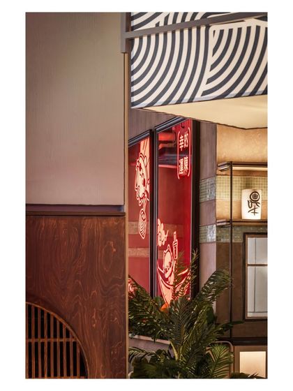 A glimpse of the red neon mascot signage seen through a wooden framed interior window. This layering effect creates intrigue and reveals different design elements as guests move through the space.