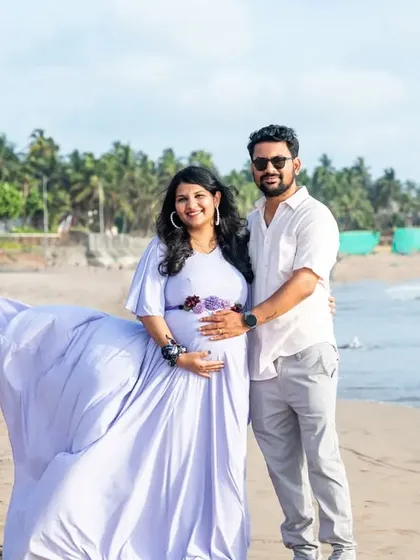 A stunning wide shot of a couple on the beach, with the wind catching the mom-to-be's lavender gown, creating a beautiful, flowing silhouette.