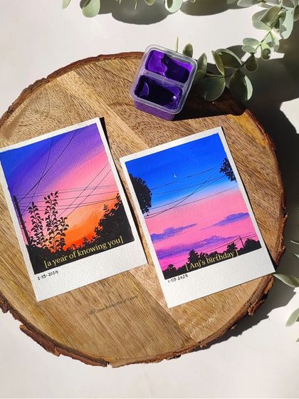 Two custom polaroid paintings of sunset skies, one with deep purples and oranges, and another with soft pinks and blues.