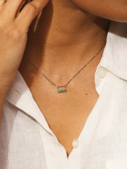 The Petit Emerald necklace worn up close, highlighting the simple bar of three emeralds on a fine gold chain.