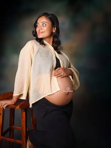 A glowing and natural bare-bump portrait. The focus here is on the mother's happy expression and the beautiful shape of her belly, captured with soft studio lighting against a classic backdrop.