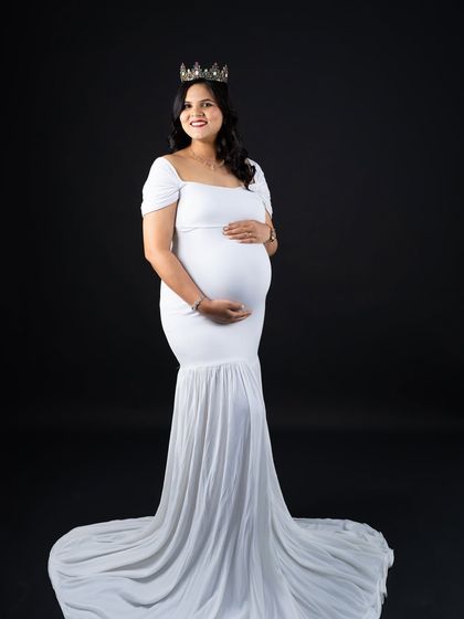 Simple, pure, and angelic. A classic white mermaid gown paired with a crown against a solid black backdrop creates a striking and timeless maternity portrait.