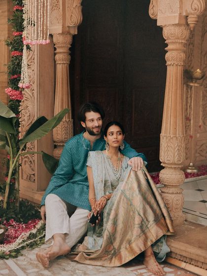 Seated together in a beautifully decorated doorway, this couple shares a moment of calm. The composition draws the eye to their connection, framed by the architectural details and floral arrangements of their chosen venue.