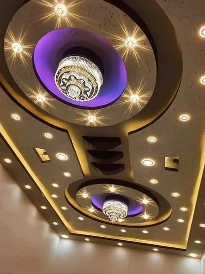 A grand ceiling design featuring two large chandeliers set within recessed circular sections. The purple accent lighting adds a touch of modern royalty to the classic warmth of the spotlights.