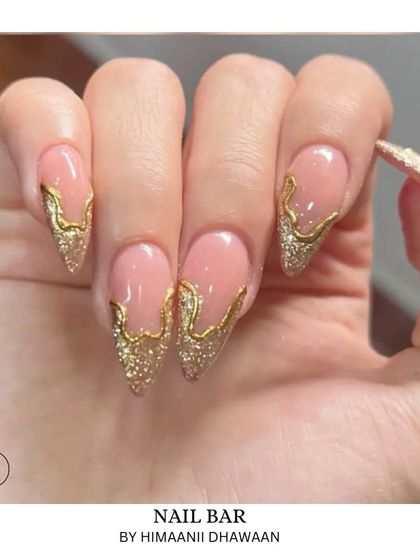 Pointed stiletto nails with a nude base, featuring a dramatic gold glitter drip effect. A bold and artistic statement.