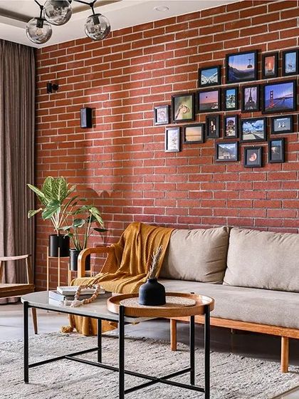 A wider view of the living room, showing the full effect of the brick feature wall and the gallery of travel photos. The layout is designed to be open and comfortable, with a clear connection to the outdoor space.