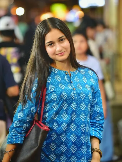 A confident and direct portrait. Her calm expression and the lively, blurred background create a striking contrast in this night street photograph.