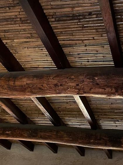 The ceiling detail of the Hassan farmhouse, combining thick, rustic wooden beams with a layer of woven bamboo for a textured, natural finish.