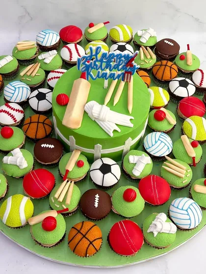 A vibrant, custom-designed sports-themed birthday celebration platter. It features a central cricket-themed cake surrounded by dozens of mini cupcakes decorated as soccer balls, basketballs, tennis balls, and more, showing our creative range for themed parties.