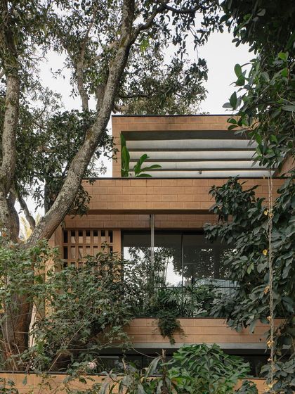 The Debris Block House is nestled among mature trees. The design uses stepping volumes and integrated planters to make the building feel like a part of the lush landscape.