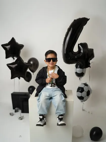 Posing with confidence, this little guy shows off his fourth birthday swag. The black and white theme with footballs and stars creates a modern and fun atmosphere.