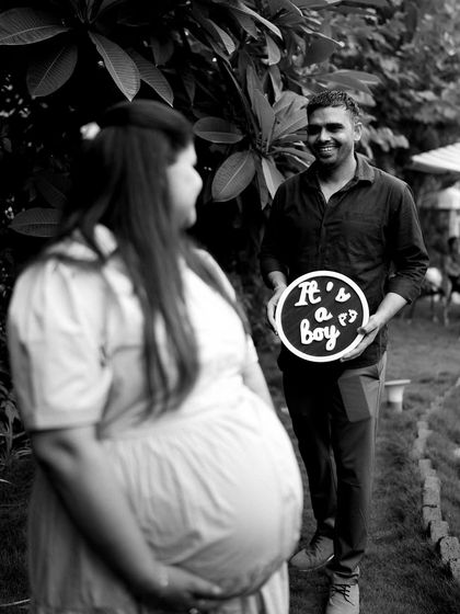A sweet gender reveal moment. The dad-to-be holds an "It's a boy" sign, with the mom's baby bump in the foreground. The focus creates a sense of anticipation and surprise.