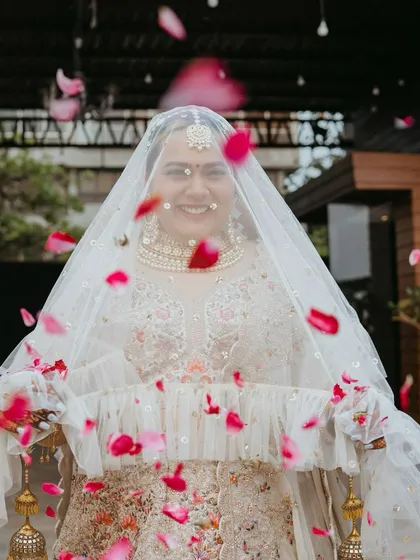 A beautiful bridal entry shot, with the bride smiling through her veil as rose petals shower down on her. A moment of pure joy and celebration.