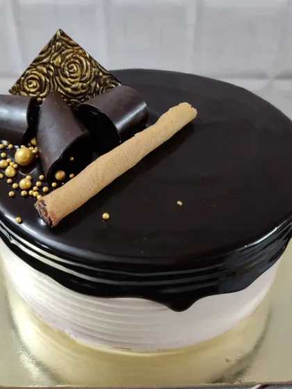 This chocolate drip cake is all about rich flavors and elegant decoration. It's topped with dark chocolate curls, golden sugar beads, a decorative chocolate piece, and a crunchy wafer roll.