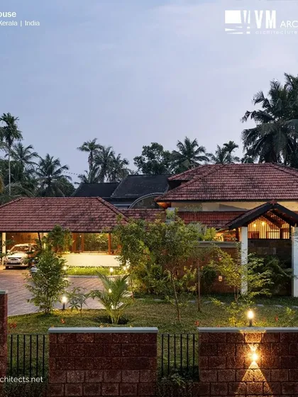 The exterior of Kuttiyil House at dusk, where the design truly comes alive. The sloped terracotta roofs, laterite walls, and warm landscape lighting work together to create an inviting and majestic presence, showcasing how traditional architecture can be both grand and grounded in nature.