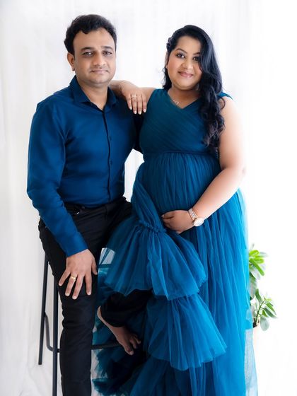 A relaxed and confident portrait of a couple, with the mom-to-be in a stunning blue gown and her partner seated beside her.