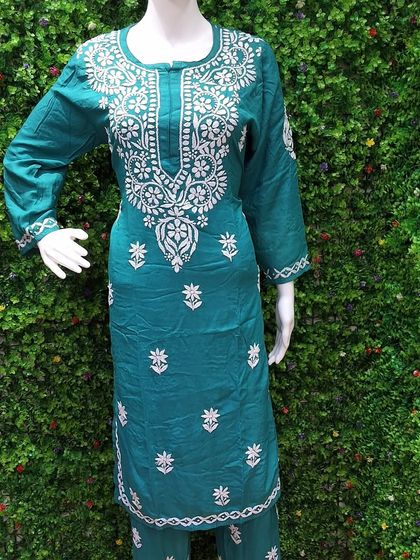 This teal green Chikankari suit set is displayed on a mannequin, showing the complete look with matching pants. The delicate white embroidery stands out against the rich color of the cotton fabric.