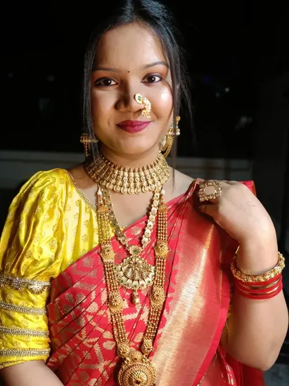 A close-up portrait of the bride. Her makeup features a bold lip and defined eyes, complemented by heavy traditional gold jewellery, including a nath and choker.