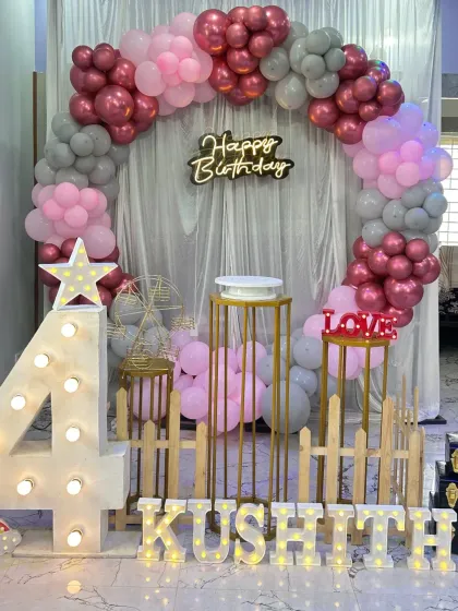 A beautiful circular balloon arch in pink, grey, and rose gold. The setup includes a large light-up number '4', a small fence detail, and marquee letters, perfect for a stylish 4th birthday.