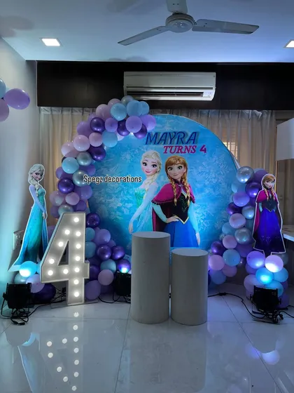 A magical Frozen-themed birthday party for a 4-year-old. This setup includes a custom circular backdrop with Anna and Elsa, life-sized character cutouts, a light-up marquee number, and a balloon arch in a wintery color palette.