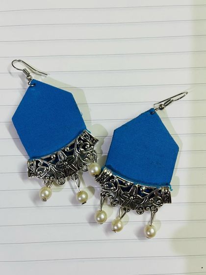 These fabric earrings feature a solid blue base in a unique geometric shape, adorned with an oxidised silver charm and pearl drops.