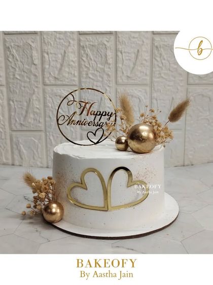 Pure elegance. This simple anniversary cake is decorated with two golden hearts, dried flowers, and gold spheres for a rustic yet chic look.