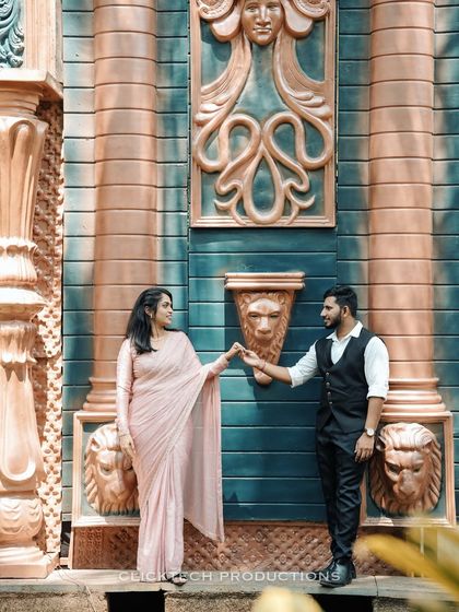 A creative pose against a wall with Greco-Roman-style carvings, the couple in traditional outfits, creating a unique fusion look.