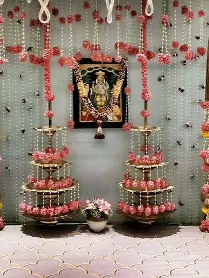 For intimate home ceremonies like a pre wedding pooja, I focus on creating a serene and beautiful spiritual space. This setup features traditional tiered brass lamps (deepastambha), delicate strings of pearls and pink flowers, and a sacred backdrop for the deity.