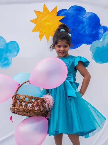 This bright turquoise dress with flutter sleeves and a large bow is designed for joyful moments. The lightweight tulle skirt is perfect for dancing and playing at any party.