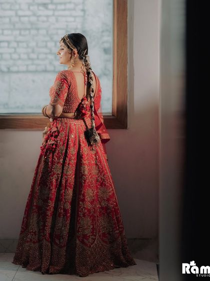 A beautiful shot of the bride from the back, highlighting her intricate hairstyle and the detailed embroidery of her red lehenga.
