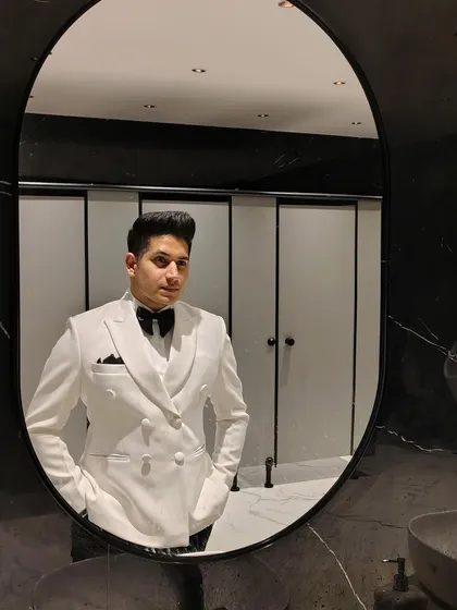 A perfect fit is everything. This client is seen in a mirror selfie wearing our pristine white double-breasted tuxedo, complete with a waistcoat, black bow tie, and pocket square for a classic, gentlemanly look.