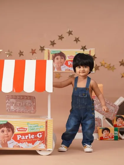 Another angle of the baby girl standing by her Parle-G stall, showcasing the complete and detailed themed setup.