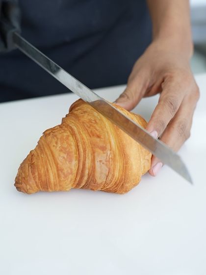 A close-up of a freshly baked croissant being sliced, revealing the delicate, airy layers inside. This is the result of patience, precision, and the right technique.
