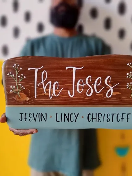 A family name plaque for "The Joses" held with pride. The design combines a rich brown wood stain with a deep teal accent and delicate, hand-painted baby's breath for a touch of class.