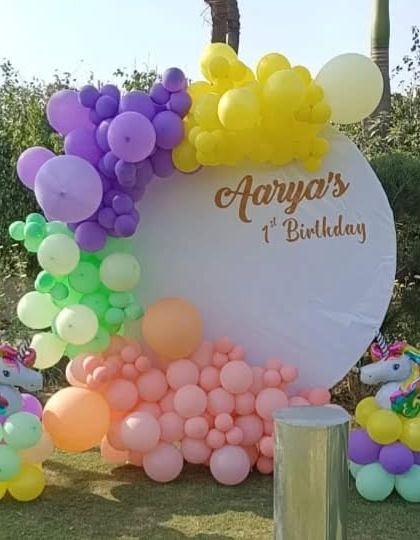 A whimsical unicorn-themed first birthday in a garden setting. The decor features a pastel balloon arch and unicorn foil balloon sculptures.