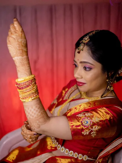 A candid moment of the bride getting ready. Her makeup, with pink eyeshadow and a bold red lip, is paired with a classic hair bun.