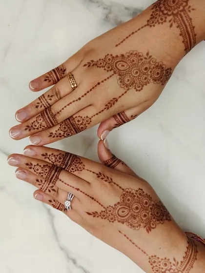 This stylish and minimal Arabic mehendi design is perfect for an engagement or party. It features delicate floral motifs connected by dotted lines, creating an elegant look on the back of the hands.