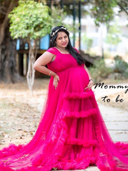 A joyful outdoor portrait of a mom-to-be in a vibrant pink ruffled gown. The natural park setting adds a relaxed and happy feel to the photograph.