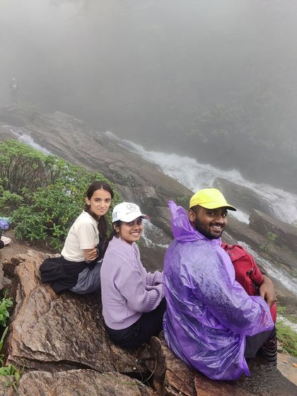 Three friends sitting at the top of Bandaje Falls, enjoying the misty view.