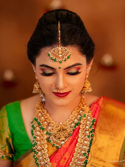 A classic beauty shot focusing on the face, makeup, and jewelry. The lighting is carefully controlled to highlight the shimmer of the gold jewelry and the rich colors of the makeup and saree.