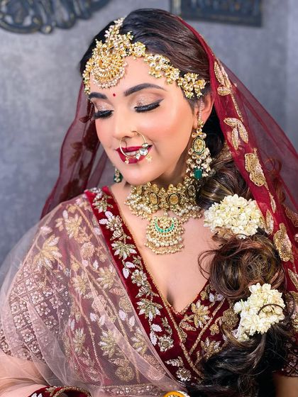 An elegant bridal portrait with eyes closed, showcasing the detailed eye makeup. The soft glitter and sharp eyeliner are the highlights, paired with a beautiful matha patti and a traditional braid with gajra.